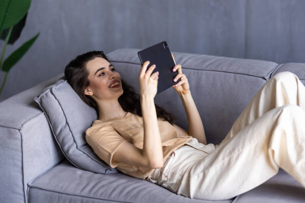 istock Beautiful young woman in casual clothes is using a digital tablet while sitting on couch at home 1699211016