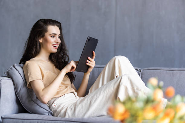 istock Beautiful young woman in casual clothes is using a digital tablet while sitting on couch at home 1699211253