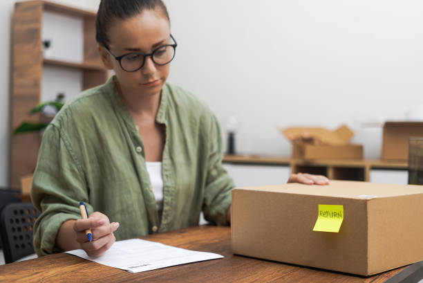 istock woman sits by table, engrossed in writing a return order and formulating product return request. 1699229733