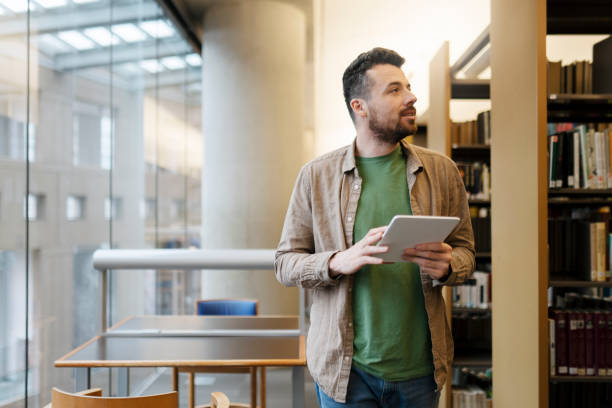 istock Handsome man stands in the university library, uses digital tablet, looks away. Latin student 1699271990