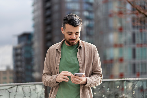 Smiling hipster man using mobile phone shopping online outdoors. Happy successful influencer holding smart phone standing on the street