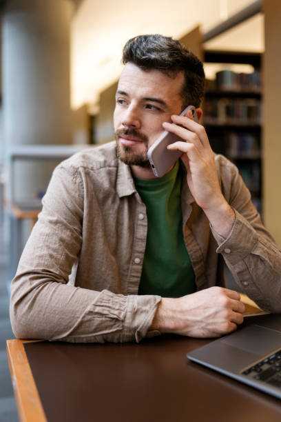 istock Hispanic businessman talking on mobile phone, using laptop sitting in office looking away 1699272027