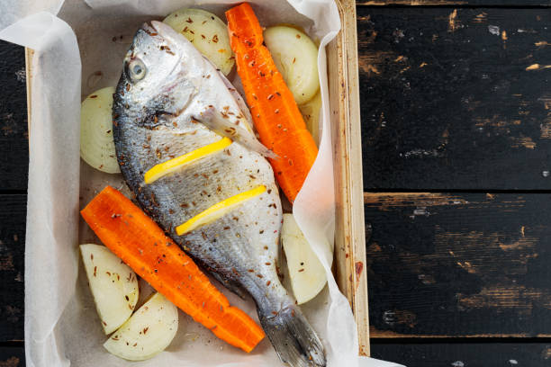 istock Raw dorado fish with lemon, vegetables and spices on parchment paper. Top view. Copy space 1699345865