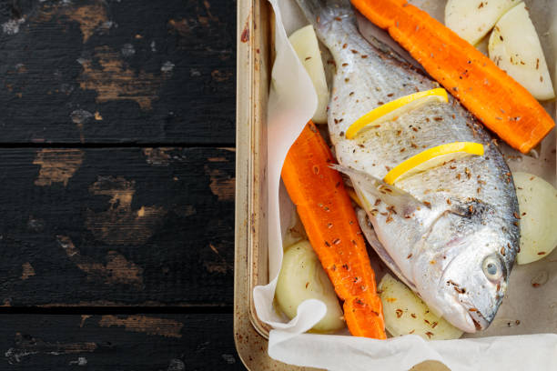 istock Raw dorado fish with lemon, vegetables and spices on parchment paper. Top view. Copy space 1699345880