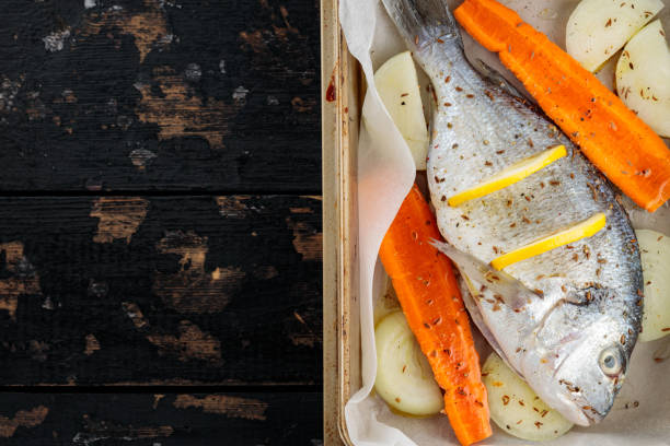 istock Raw dorado fish with lemon, vegetables and spices on parchment paper. Top view. Copy space 1699346400