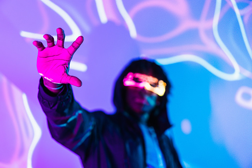 Studio portrait with purple and blue neon lights with focus on the hand of a futuristic man with AR goggles