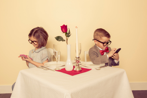 A young boy and girl are on a date, and really would rather play with their mobile devices than be with each other.