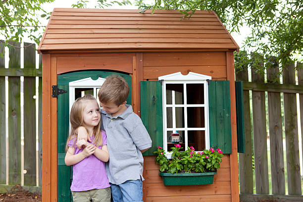 Children being friendly in front of wooden playhouse Young girl and boy with a playhouse. kids play house stock pictures, royalty-free photos & images