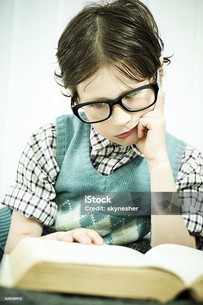 Cute geek boy reading a book. Cute looking boy wearing big black glasses is reading his book.   1970-1979 Stock Photo