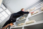 Woman on a ladder reaching for a box out of reach