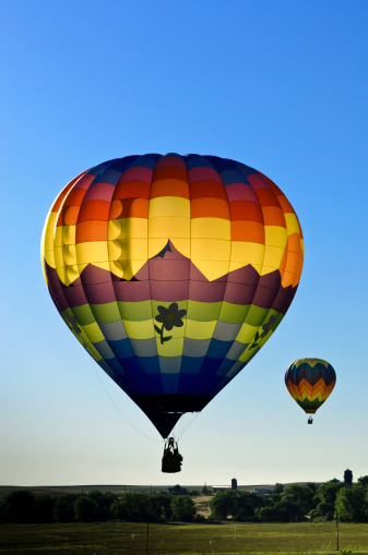 A pair of hot air balloons backlit at sunrise.