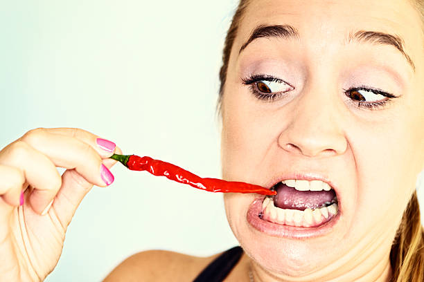 Woman displaying a red hot spicy chilli pepper or dried cayenne pepper in her hand used as a pungent aromatic seasoning in cooking with selective focus and colour of the pepper and her nail varnish