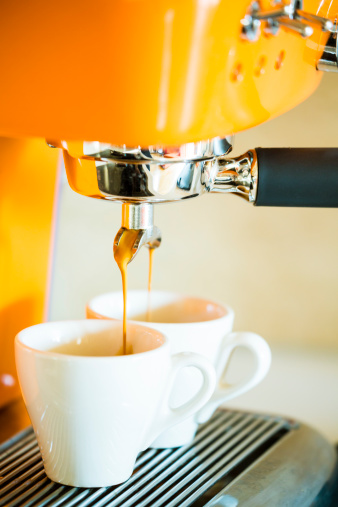 Espresso flowing from coffee machine to two small cups