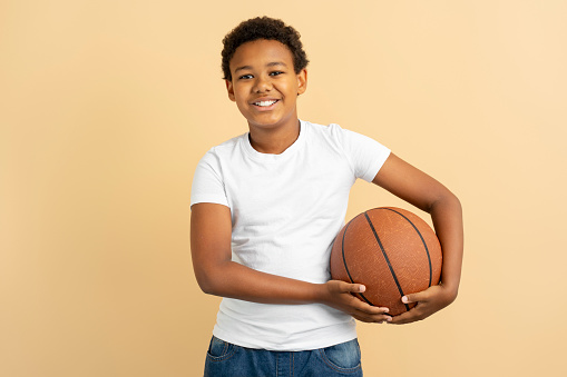 Portrait young smiling African American boy holding ball playing basketball isolated on background