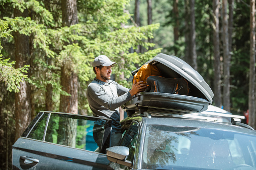 Mid adult man filling cargo box container on roof rack for camping vacation.