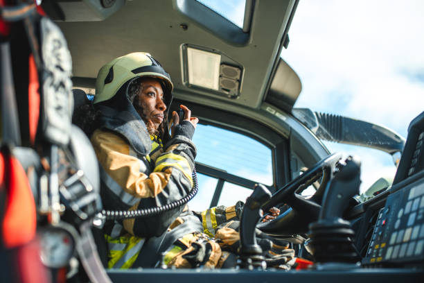 Female Firefighter Using A CB Station In A Firetruck Side view of a Black female airport firefighter sitting in a fire truck using a CB station while driving towards an emergency location at the airport runway. 8564 stock pictures, royalty-free photos & images