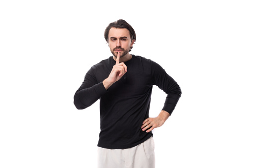 young handsome brunet european man in a black sweater keeps a secret on an isolated white background.