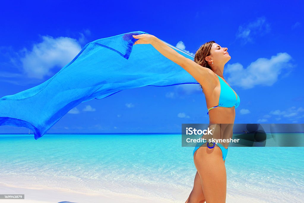 Happy woman walking on a beach with long sarong. Happy attractive woman enjoying while walking with a long blue sarong on a beach.    Activity Stock Photo