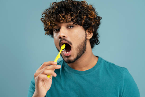 istock Handsome Asian young man brushing teeth with a yellow toothbrush, on isolated blue background 1699441626
