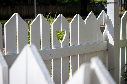 A white wooden fence around a home with heart shapes cut out.