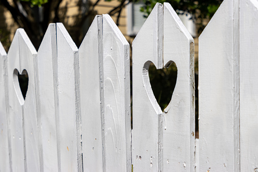 A white wooden fence around a home with heart shapes cut out.