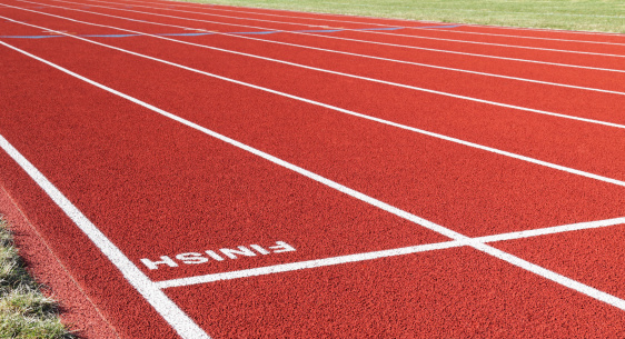 Closeup of the inverted word FINISH at the finish line on a synthetic red running track with lanes for competitive races. Shallow depth of field with focus on the finish line.