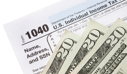 A U.S. 1040 tax form with three twenty-dollar bills.