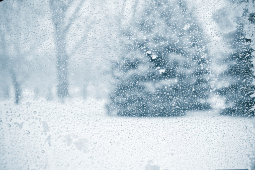 Winter wonderland seen through a wet and snowy glass window.