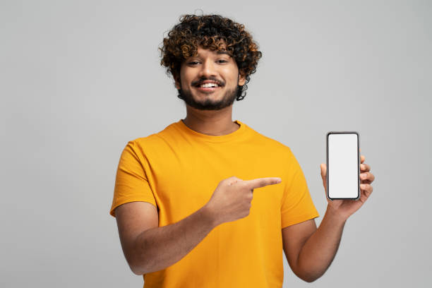 istock Smiling Indian man holding mobile phone, shopping online pointing finger at empty display, isolated 1699464124