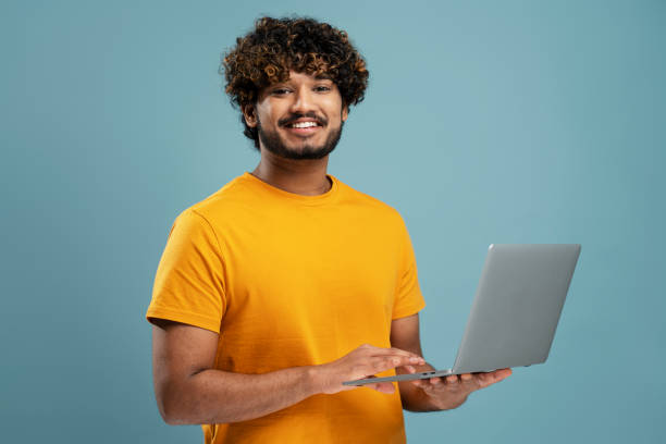 Smiling Indian man holding laptop computer working online. Portrait of happy programmer