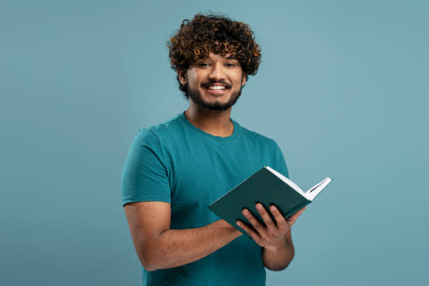 istock Smiling Indian man reading book isolated on blue background. Smart asian student studying. Education 1699464639