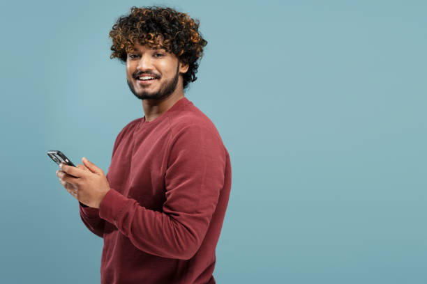 istock Smiling Indian man holding smartphone using mobile app shopping online isolated on background 1699464662