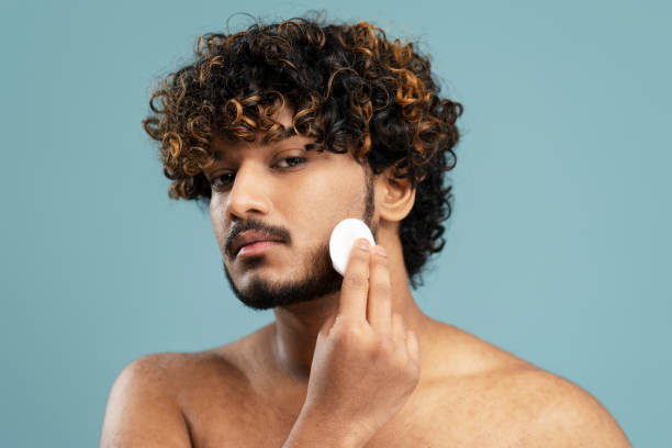 istock Indian man removing makeup using cotton disk, cleaning face, looking at mirror. Beauty, skin care 1699465172
