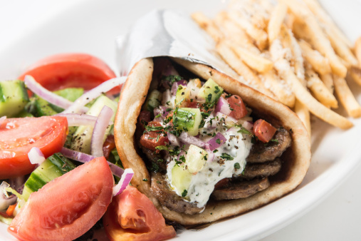 A close-up of a gyro pita sandwich with a salad and fries.