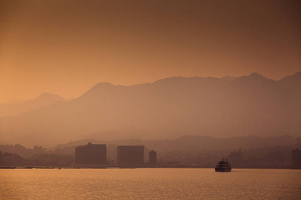 A ferry boat crosses the bay behind a very hazy Hiroshima skyline at dusk