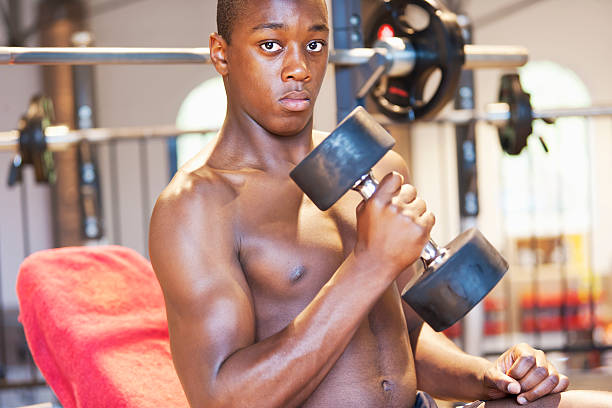 Young athlete holding dumbbell A young coloured athlete, holding a dumbbell in a fitness studio. freier oberkörper stock pictures, royalty-free photos & images