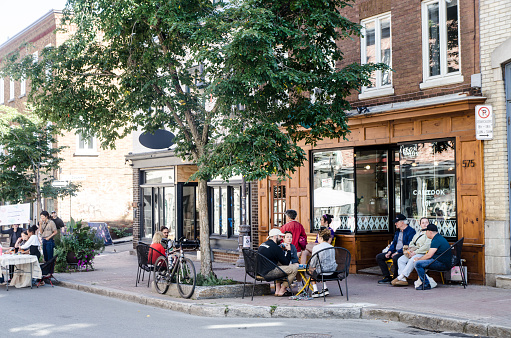 Facade of a cafe during summer day in Quebec city with people eating and drinking coffee while sitting at table on the sidewalk