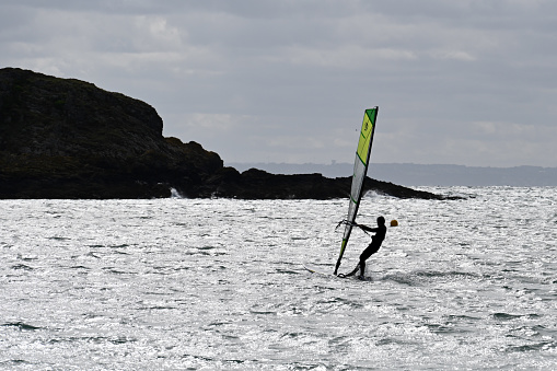 Erquy, Brittany, France, August 27, 2023 - Young man with a windsurf board in the harbor bay of Erquy.