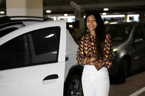 Portrait of confident smiling Indian woman, driver holding arms crossed, standing near new car