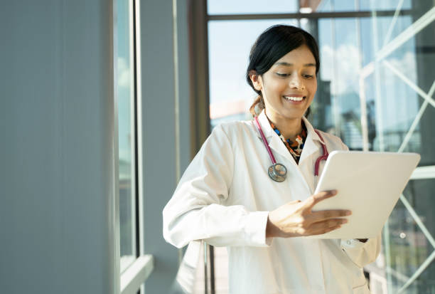 istock Smiling Indian doctor with stethoscope wearing white lab coat holding digital tablet in hospital 1699504262