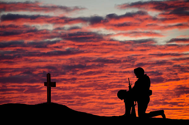 Veterans' Day Soldier A soldier kneeling in front of a grave with a cross at sunset. memorial vigil stock pictures, royalty-free photos & images