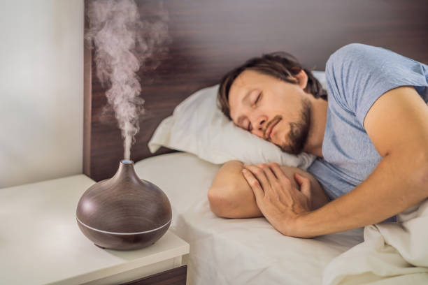 Aromatherapy Concept. Wooden Electric Ultrasonic Essential Oil Aroma Diffuser and Humidifier. Ultrasonic aroma diffuser for home. Man resting at home stock photo
