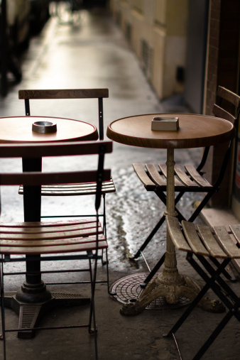 Empty tables and chairs on the sidewalk in front of a Parisian cafe. Shallow focus.