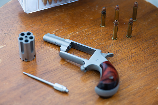 This is a photograph of a disassembled 22 caliber revolver gun with an empty barrel and bullets on a distressed wooden table top in Florida, USA.