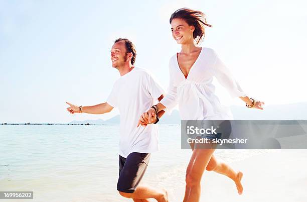 Feliz Pareja Sosteniendo Las Manos Y Disfrutar De Corriendo En La Playa Foto de stock y más banco de imágenes de Azul