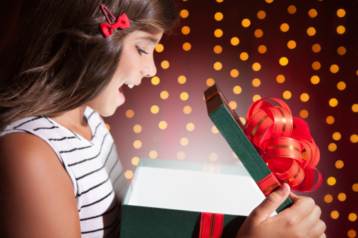 Cute exited girl opening gifts over red background with bokeh.