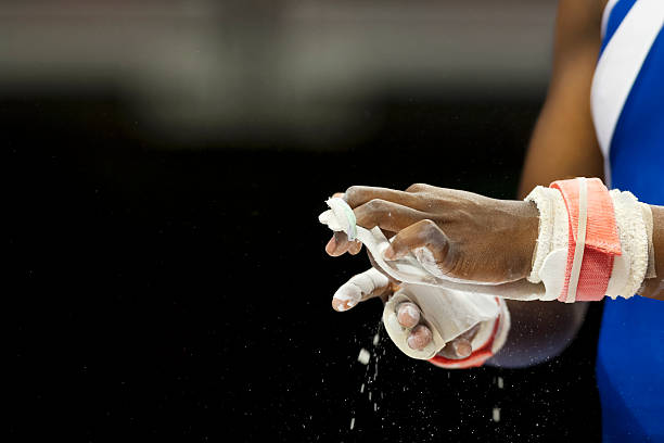 Female Gymnast prepare for competition Close-up of an African American female gymnast rubbing hands covered in chalk as she prepares for competition against a dark background gymnastics stock pictures, royalty-free photos & images