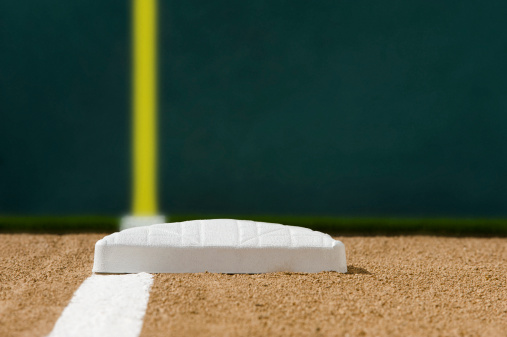 A low angle look up the third baseline with new white chalk, with the yellow foul line and green left field wall in the backgound.