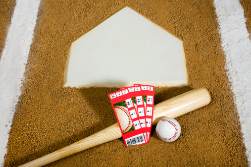 Three Baseball ticket stubs sitting against a wooden bat at Home Plate with the chalk lines of the batter's box
