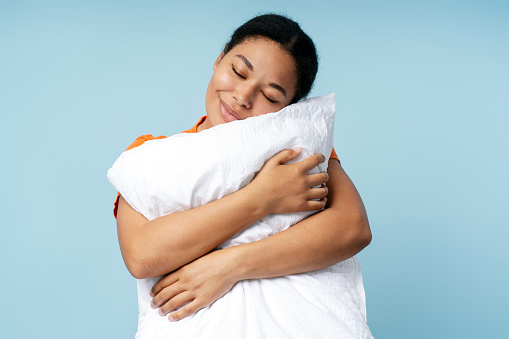 Happy African American woman sleeping, holding white pillow isolated on blue background. Morning concept